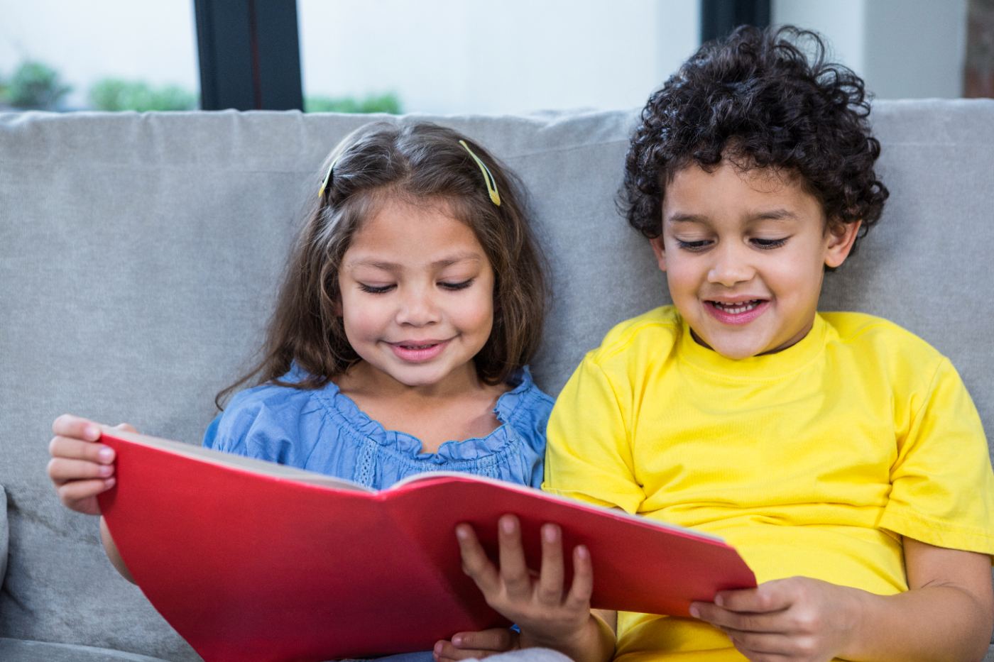 Dos hermanos leyendo un libro rojo en el sofá
